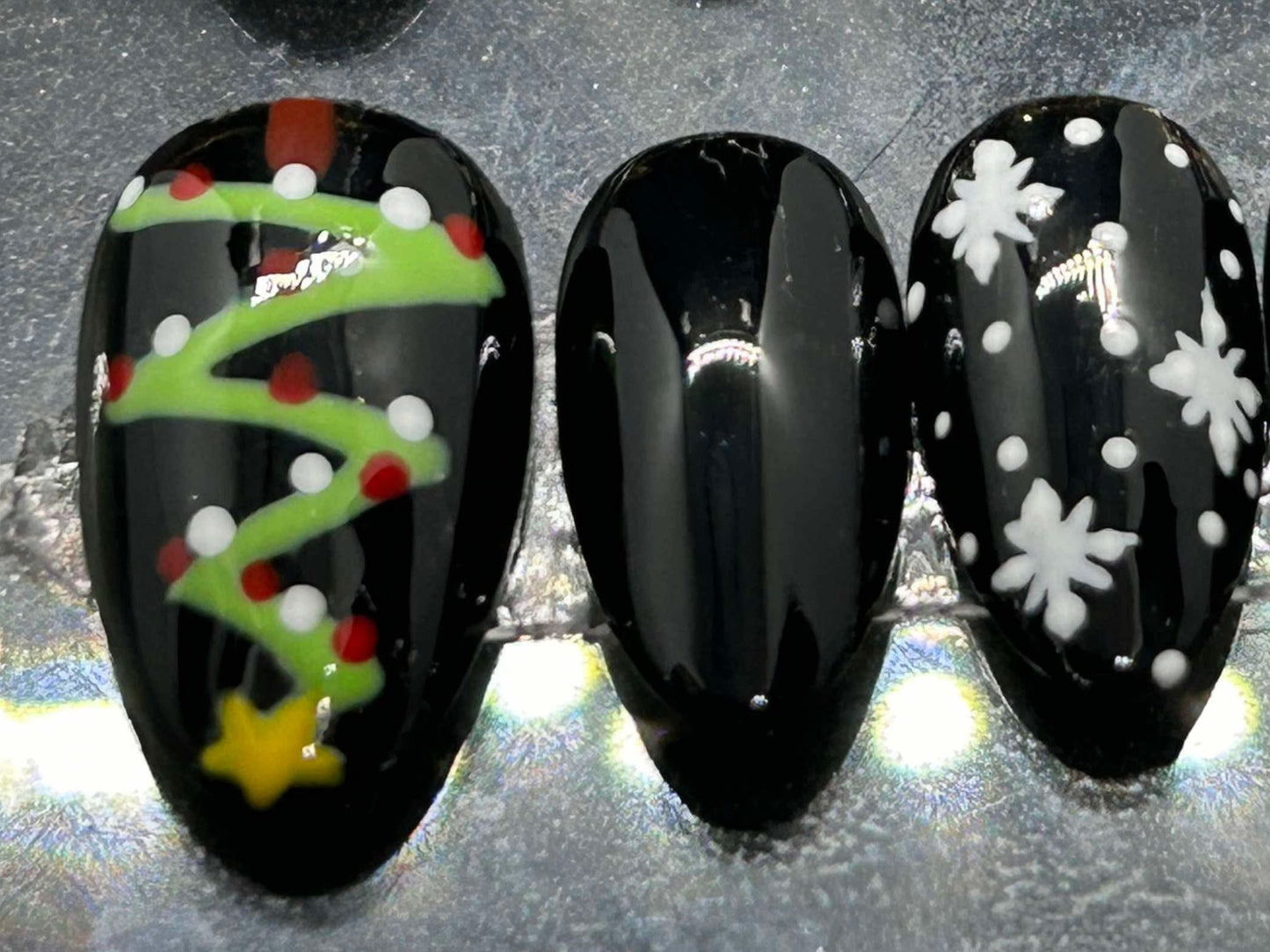 A festive set of glossy gel press-on nails featuring Christmas trees, snowflakes, and red gift bows with rhinestone accents. Displayed in a clear case, the nails come in various sizes and shapes, perfect for holiday glam.