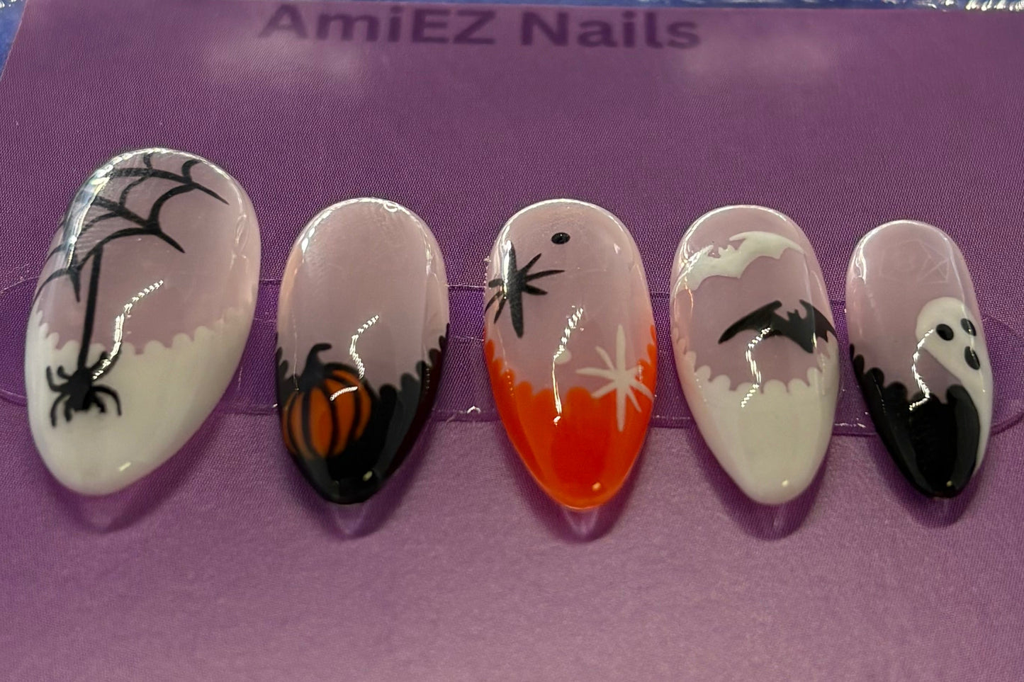 Set of decorative false nails with spider designs in a clear case on a purple background